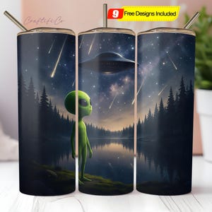 May include: Three stainless steel tumblers with a design of a green alien looking up at a flying saucer in a starry night sky with shooting stars. The tumblers are in a forest setting with trees and a lake.