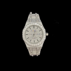 May include: A silver wristwatch with a diamond-encrusted bezel and strap. The watch face is silver with black hour markers and hands. The watch features a date display and a crown on the right. The background is black.