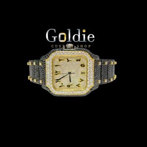 May include: A luxury wristwatch with a gold-coloured face and a black and gold band. The watch face is square with diamond accents and Arabic numerals. The watch is set against a black background, with the text "Goldie Custom Shop" above it.