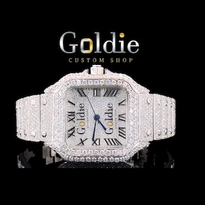 May include: A diamond-encrusted wristwatch with a square face and a matching band. The watch face displays Roman numerals and the brand name "Goldie". The image is set against a black backdrop, accentuating the watch's sparkle.