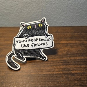 May include: Black cat holding a sign that says "Your poop smells like flowers".