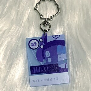 May include: A blue and purple character with a skull on its head is featured on a keychain. The character is holding a microphone and has a music note symbol on its chest. The keychain is made of clear acrylic and has a silver metal ring.
