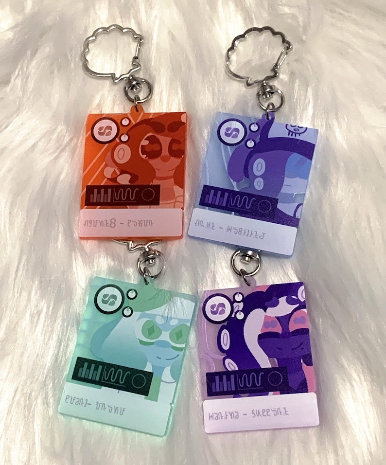 May include: Four colorful acrylic keychains featuring cartoon characters with different colored backgrounds. Each keychain has a silver ring and a graphic of a sound wave with the text "SUPER" and a character name.