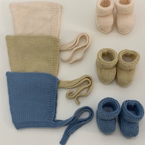 May include: Three knitted baby hats in beige, green, and blue with matching knitted booties in the same colours.