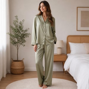 May include: Sage green pajama set. The set includes a button-down shirt with a notched collar and long sleeves, and matching wide-leg pants. The pajamas are made of a silky material and are designed for comfort and relaxation.