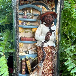 May include: A miniature dollhouse scene inside a lantern, featuring a woman with a broom and a shelf filled with bottles and books. The scene is painted in warm colors and has a whimsical, magical feel.