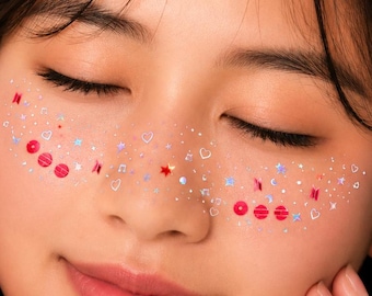 May include: A set of adhesive face stickers featuring a variety of small holographic shapes including red circles, stars, hearts, and musical notes, applied across the bridge of the nose and cheeks, complemented by a white pearl-embellished star hair clip.
