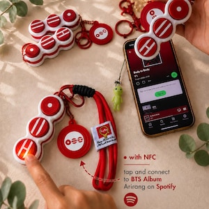 May include: A red and white fidget keychain featuring three circular buttons with symbols, a round charm, and a red lanyard. The device includes NFC technology to connect to the BTS Album Arirang on Spotify. A small green alien charm is attached.