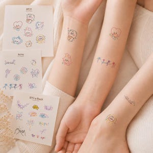 Peut inclure: Trois feuilles blanches de tatouages temporaires présentant des illustrations colorées de personnages BT21, des logos BTS et du texte comme Army et BTS is Back. Plusieurs de ces petits motifs délicats sont appliqués sur trois avant-bras.