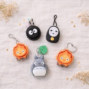 Può includere: Una collezione di portachiavi con personaggi di film d'animazione popolari. I portachiavi includono uno sprite di fuliggine nero, uno spirito Senza Volto, un Calcifer e un Totoro grigio. Ogni portachiavi ha una catena di metallo.