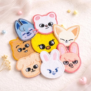 May include: A collection of eight embroidered fabric patches featuring stylized animal faces in various colors including white, yellow, light blue, tan, and pink. Each patch displays a unique cartoon-like character with distinct facial expressions.