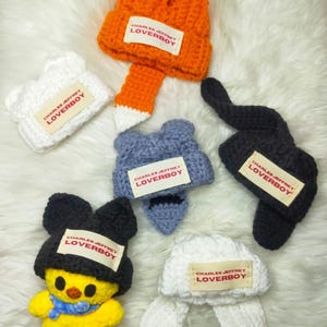 May include: Six crocheted hats with ear flaps, each featuring a different color and animal design. The hats have a label that reads "CHARLES JEFFREY LOVERBOY".