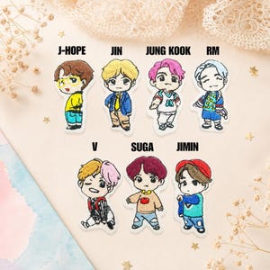 Puede incluir: Siete parches bordados con figuras estilo caricatura etiquetadas como J-HOPE, JIN, JUNG KOOK, RM, V, SUGA y JIMIN. Cada figura muestra colores de cabello distintos, incluyendo marrón, amarillo, rosa, azul y rojo, vistiendo ropa casual colorida.