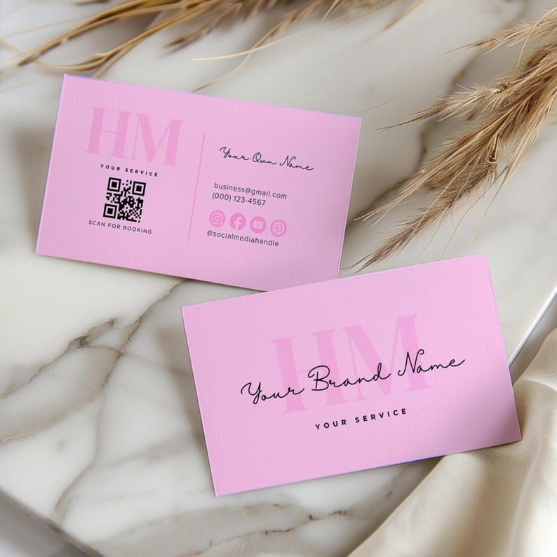 Op de afbeelding: Twee roze visitekaartjes met de initialen "HM" in een vet, zwart lettertype. De bovenste kaart heeft de tekst "Your Own Name", "business@gmail.com", "(000) 123-4567" en "@socialmediahandle". De onderste kaart heeft de tekst "Your Brand Name" en "YOUR SERVICE". Beide kaarten hebben een QR-code en de tekst "SCAN FOR BOOKING".