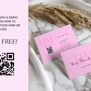 Op de afbeelding: Twee roze visitekaartjes met de tekst "HM" en "Your Brand Name" in roze lettertype. De kaartjes liggen op een wit marmeren oppervlak met een gedroogde grasspriet.