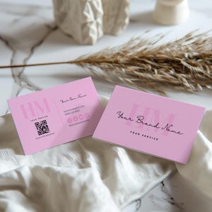 Op de afbeelding: Twee roze visitekaartjes met de tekst "HM YOUR SERVICE" en een QR-code op de ene kaart en "Your Brand Name YOUR SERVICE" op de andere kaart.