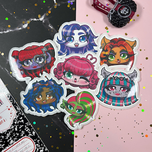 Peut inclure: Une collection d'autocollants colorés de style dessin animé représentant divers personnages sur le thème des monstres avec des coiffures et des traits du visage uniques. Les autocollants ont une finition brillante et sont disposés sur un fond noir et rose.