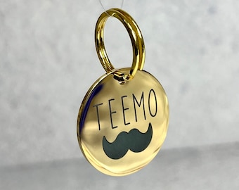 May include: Gold-colored round pet tag with a black mustache and the name "TEEMO" engraved on it.