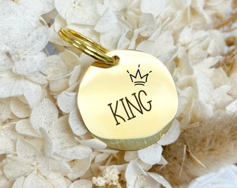 May include: Gold-colored round dog tag with a crown and the word "KING" engraved on it.