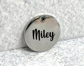May include: A silver round pet tag with the name "Miley" engraved in black lettering.