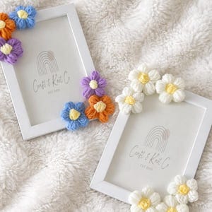 May include: Two white rectangular picture frames featuring crocheted flower embellishments. One frame is decorated with blue, orange, and purple flowers, while the other features white flowers. Both frames contain a logo reading Craft & Knot Co EST 2020.