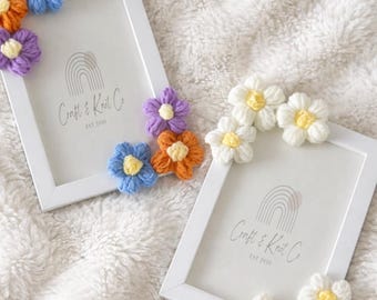 Puede incluir: Dos marcos de fotos rectangulares blancos con un logotipo de arcoíris impreso y el texto Craft & Knot Co EST 2020. Un marco está decorado con flores de ganchillo azules, naranjas y moradas, mientras que el otro tiene flores blancas.