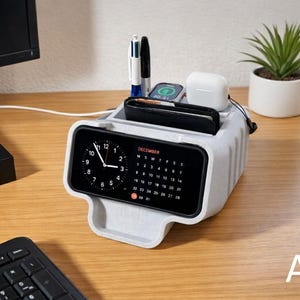 May include: A light gray desk organizer with a built-in digital clock and calendar. It holds pens, a phone, smartwatch, and wireless earbuds. A small potted plant sits nearby. The letter "A" is visible in the bottom right corner.