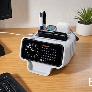 Puede incluir: Un organizador de escritorio gris claro con un reloj digital y calendario integrados. Cuenta con compartimentos para bolígrafos, una cartera, un reloj inteligente y auriculares inalámbricos. Una pequeña planta en maceta está cerca. El reloj marca las 10:09.