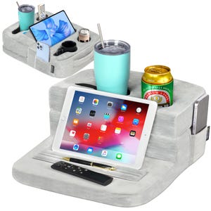 May include: A gray, cushioned bed tray with a built-in tablet holder, cup holders, and a remote control holder. The tray is holding a tablet, a can of beer, a glass of water, and a remote control.