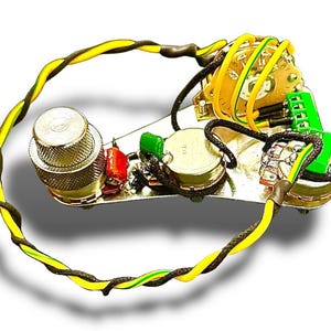 May include: A guitar wiring harness with various electronic components, including potentiometers, a switch, and capacitors. The wiring features yellow and black twisted wires, and green and red components. The components are mounted on a silver plate.