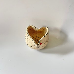 May include: A white ceramic heart-shaped bowl with black speckles and a small red heart on the side.