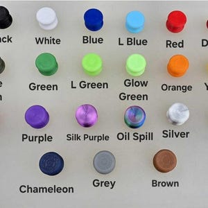 Puede incluir: Una colecci&oacute;n de tapones coloridos en varios tonos, incluyendo negro, blanco, azul, rojo y verde. Cada tap&oacute;n est&aacute; etiquetado con su nombre de color correspondiente, como "Rosa", "Morado" y "Dorado".