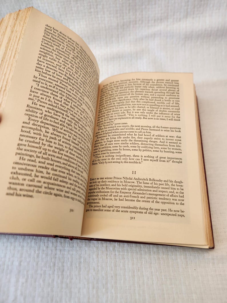 Peut inclure: Un livre reli&eacute; ouvert avec des pages couleur cr&egrave;me et du texte imprim&eacute; en noir. La page de gauche porte le num&eacute;ro 310 et la page de droite le num&eacute;ro 311, commen&ccedil;ant par le chiffre romain II et un paragraphe sur le prince Nikola&iuml;.