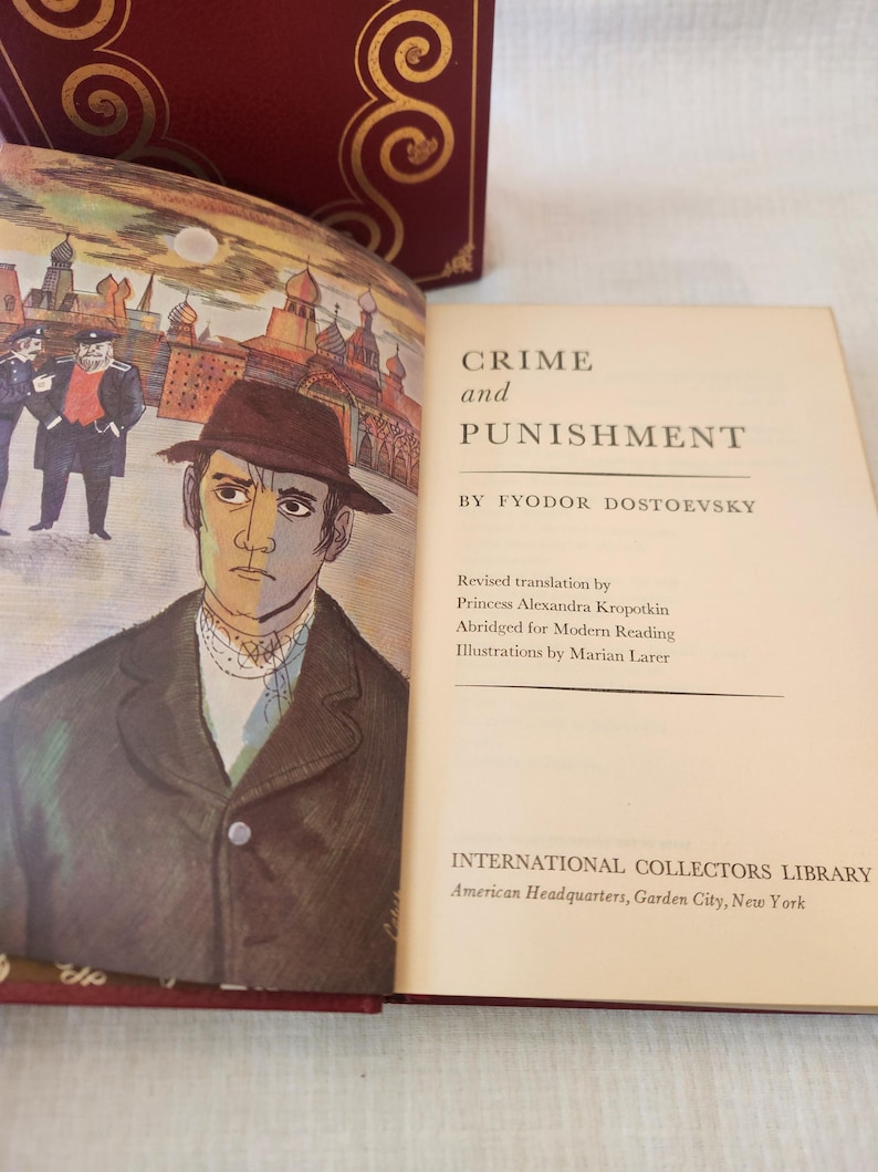 Peut inclure: Un livre reli&eacute; intitul&eacute; Crime and Punishment de Fyodor Dostoevsky, publi&eacute; par International Collectors Library. La page ouverte pr&eacute;sente une illustration d'un homme au chapeau et une sc&egrave;ne urbaine, avec le texte d&eacute;taillant la traduction et l'illustrateur.