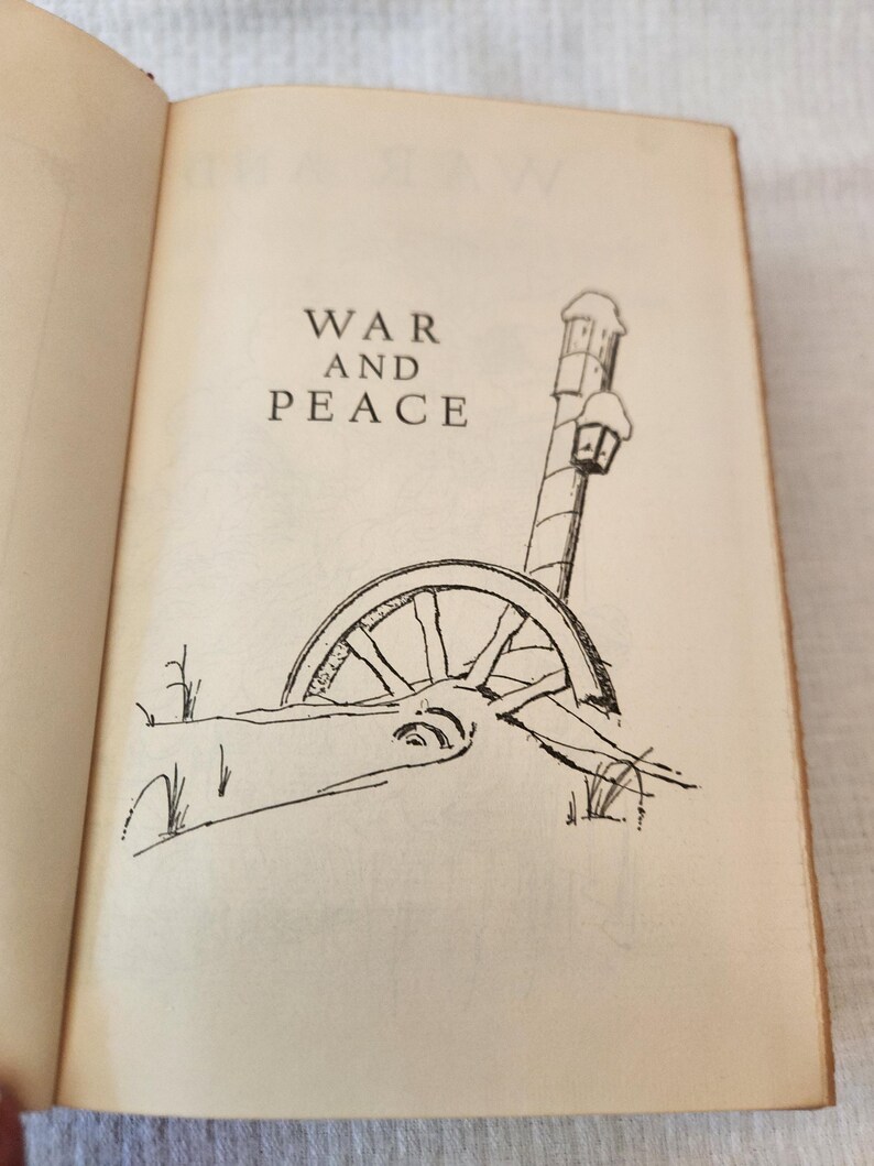Peut inclure: Une page de livre ouverte pr&eacute;sentant le titre War and Peace en texte noir. Sous le titre se trouve un dessin au trait en noir et blanc d'une roue de chariot en bois partiellement enfouie dans la neige pr&egrave;s d'un r&eacute;verb&egrave;re enneig&eacute;.