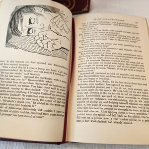 Peut inclure: Un livre reli&eacute; ouvert intitul&eacute; Crime and Punishment avec une couverture rouge fonc&eacute; et des accents d&eacute;coratifs dor&eacute;s. La page de gauche pr&eacute;sente une illustration &agrave; l'encre noire et blanche d'une personne allong&eacute;e, et la page de droite du texte.