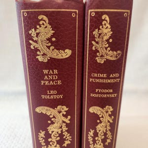 Peut inclure: Deux livres reli&eacute;s bordeaux avec des lettres dor&eacute;es et des motifs en filigrane sur les tranches. Le livre de gauche est intitul&eacute; War and Peace de Leo Tolstoy, et le livre de droite est intitul&eacute; Crime and Punishment de Fyodor Dostoevsky.