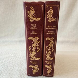 Peut inclure: Deux livres &agrave; couverture rigide bordeaux avec des lettres dor&eacute;es en relief et des motifs d&eacute;coratifs en filigrane sur les tranches. Le livre de gauche est War and Peace de Leo Tolstoy, et celui de droite est Crime and Punishment de Fyodor Dostoevsky.