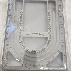 May include: A gray plastic bead design board with numbered compartments and a circular design area. The board is labeled "Bead Design Board".