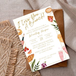 May include: A bridal shower invitation with the text "I Love You A Brunch!" in gold script. The invitation features watercolor illustrations of brunch items like a croissant, coffee, and fruit. The invitation is on a white background with a brown envelope.