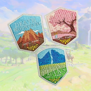 Puede incluir: Tres parches bordados con diseños de parques nacionales del videojuego The Legend of Zelda: Breath of the Wild. Los parches son blancos con un borde blanco y presentan el texto "Death Mountain Natl. Park", "Satori Mountain Natl. Park" y "Dueling Peaks Natl. Park".