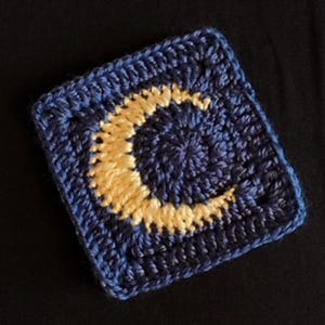May include: A crocheted square with a crescent moon design. The moon is made of a light yellow yarn and the background is a dark blue yarn.