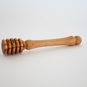 May include: A wooden honey dipper with a rounded handle and a spiral design at the end. The dipper is made of light brown wood.
