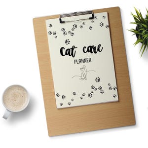 Może przedstawiać: Klip z kremowym papierem z czarnymi odciskami łap i napisem "cat care PLANNER" w odręcznej czcionce. Pod tekstem znajduje się rysunek kota. Na zdjęciu znajduje się również filiżanka kawy i mała roślina.