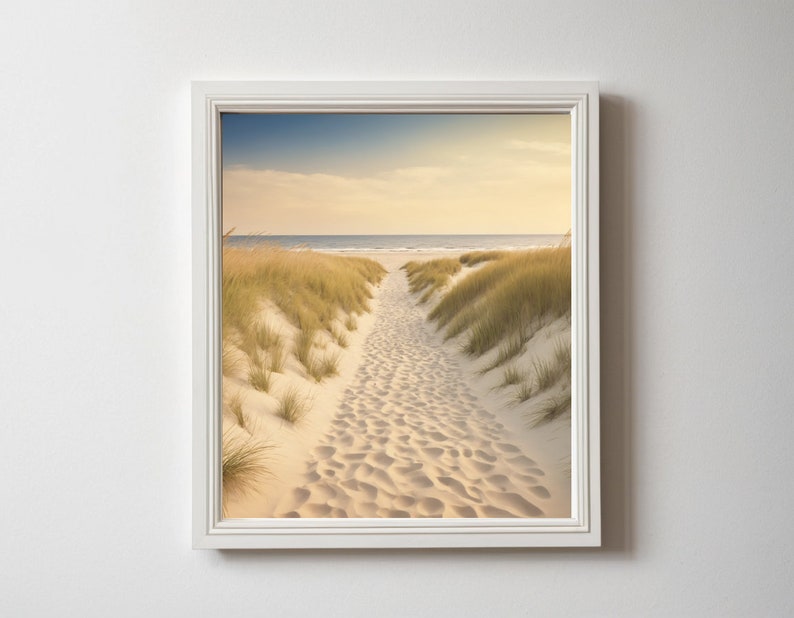 May include: A framed photograph of a sandy path leading to the ocean. The path is lined with tall grass and the ocean is in the distance. The sky is a light blue with some clouds.