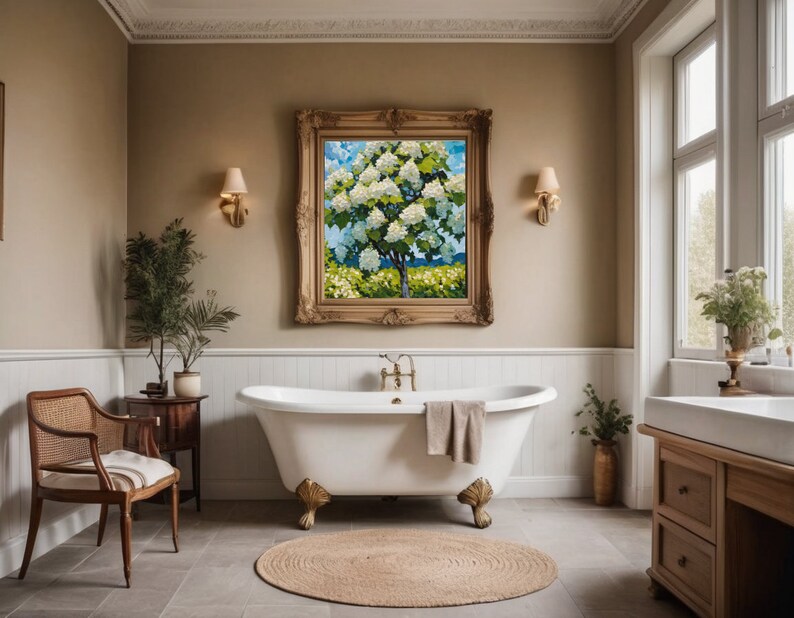May include: A white clawfoot bathtub with a towel draped over the edge, set in a bathroom with a large framed painting of a flowering tree, a wooden side table with a potted plant, and a wooden vanity with a white sink and drawers.