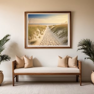 May include: A light wood bench with two beige cushions sits in front of a framed photograph of a sandy path leading to the ocean. Two potted palm trees flank the bench.