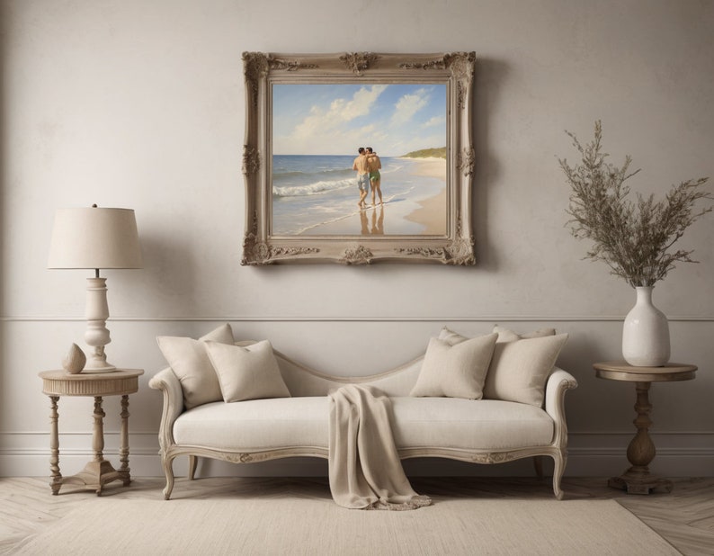 May include: A framed painting of two people walking on a beach. The painting is in a light wood frame with ornate details. The painting is hanging on a white wall above a white couch.