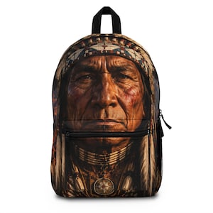Op de afbeelding: Een rugzak met een hoge resolutie print van een oudere inheemse persoon die een traditionele verentooi, een kralenketting en een cirkelvormige hanger draagt. De tas heeft een zwart handvat, zwarte ritsen en zijvakken van gaas.