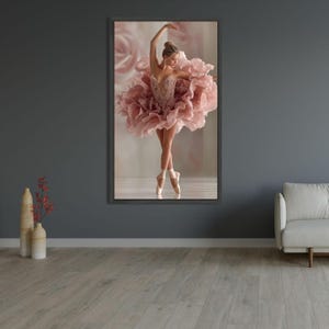Może przedstawiać: Oprawiony wydruk baletnicy w różowej, pofałdowanej sukience, en pointe. Tancerka jest w wdzięcznej pozie, z uniesioną jedną ręką. Tło przedstawia miękki, rozmyty obraz róż.